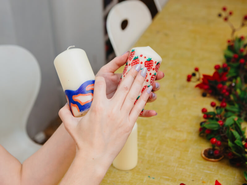 Hands holding two painted cylindrical candles